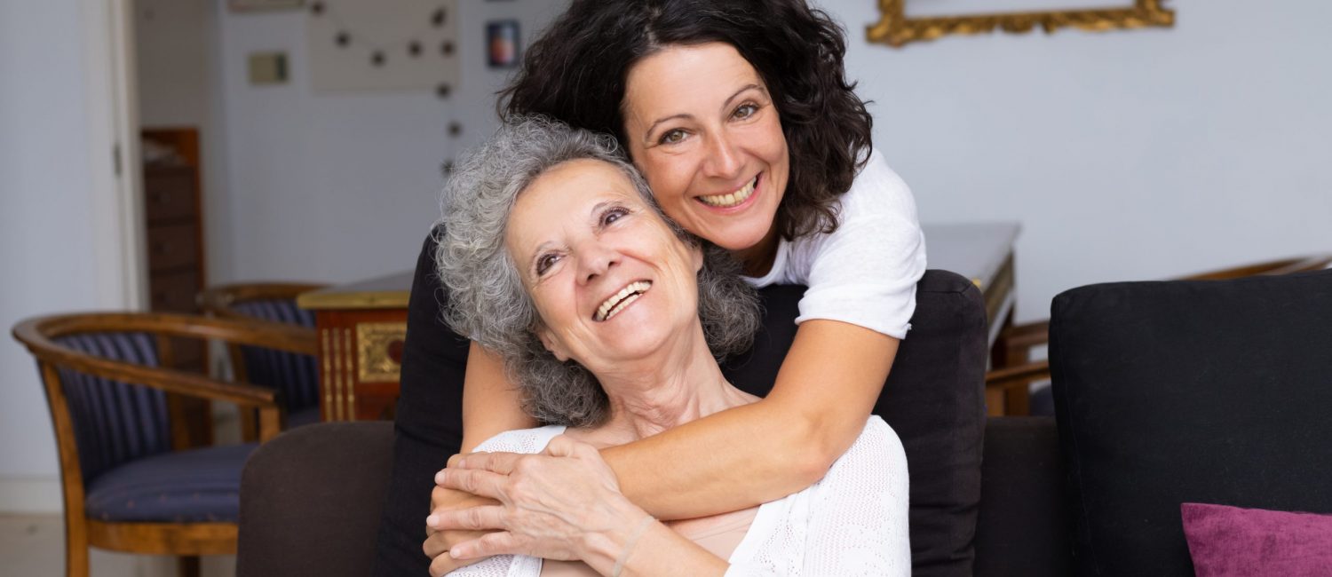 Happy middle aged woman hugging senior lady in living room. Mother and daughter embracing each other at home. Happy family concept